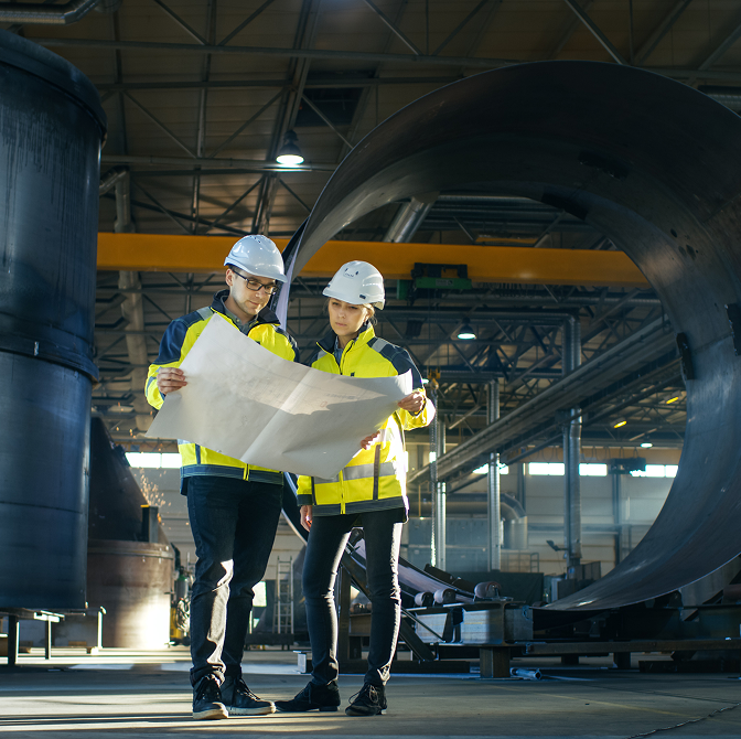 Zwei Personen mit Schutzhelmen stehen vor einem großen Rohr.