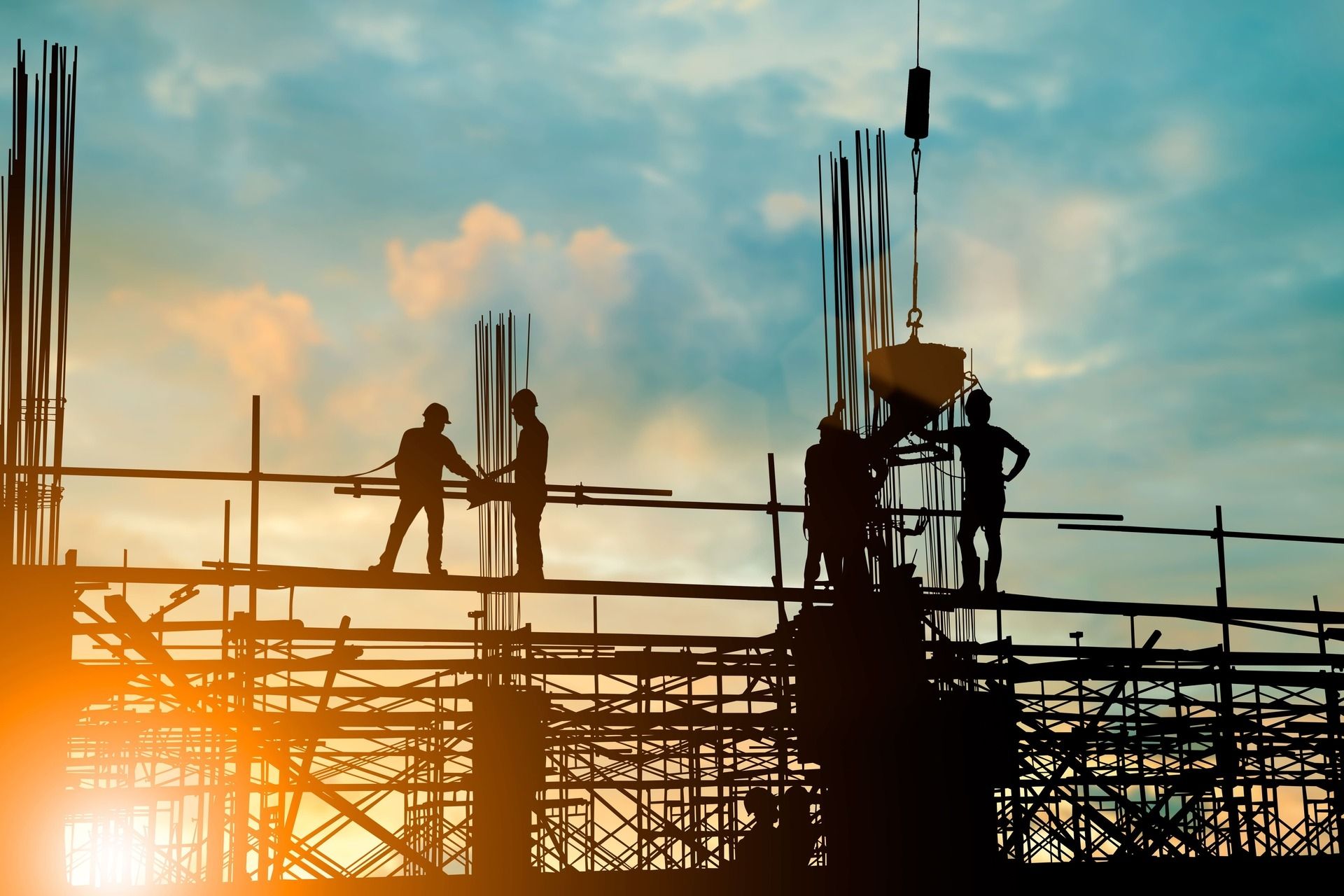 Bauarbeiter auf Gerüst bei Sonnenuntergang, die Silhouetten vor einem farbenfrohen Himmel bilden.