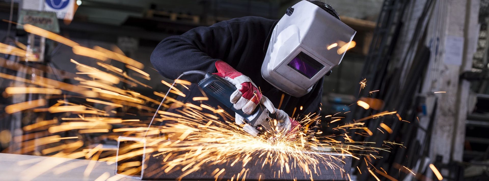 Ein Mann mit Schweißhelm, der Metall schleift, um präzise und saubere Kanten zu erzeugen.