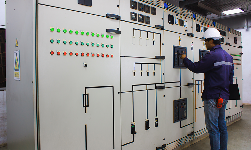 Ein Mann mit einem Schutzhelm steht vor einem Bedienfeld.